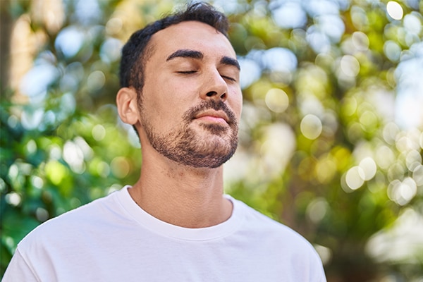 Young hispanic man breathing with closed eyes at park