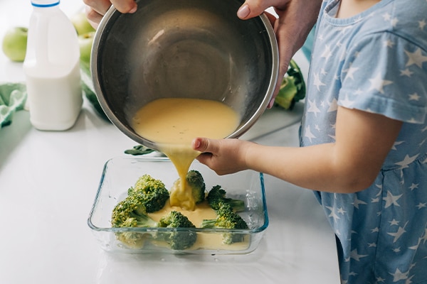 Mom teaches her little daughter how to make an omelet with vegetables.