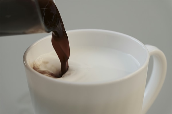 Mug of milk with hot cocoa pouring in