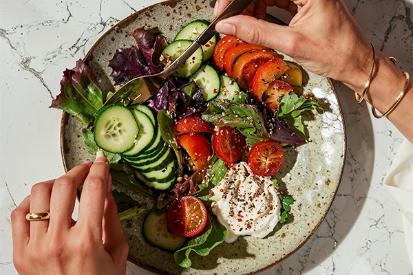 Hands holding fork cutting up vegetables on plate
