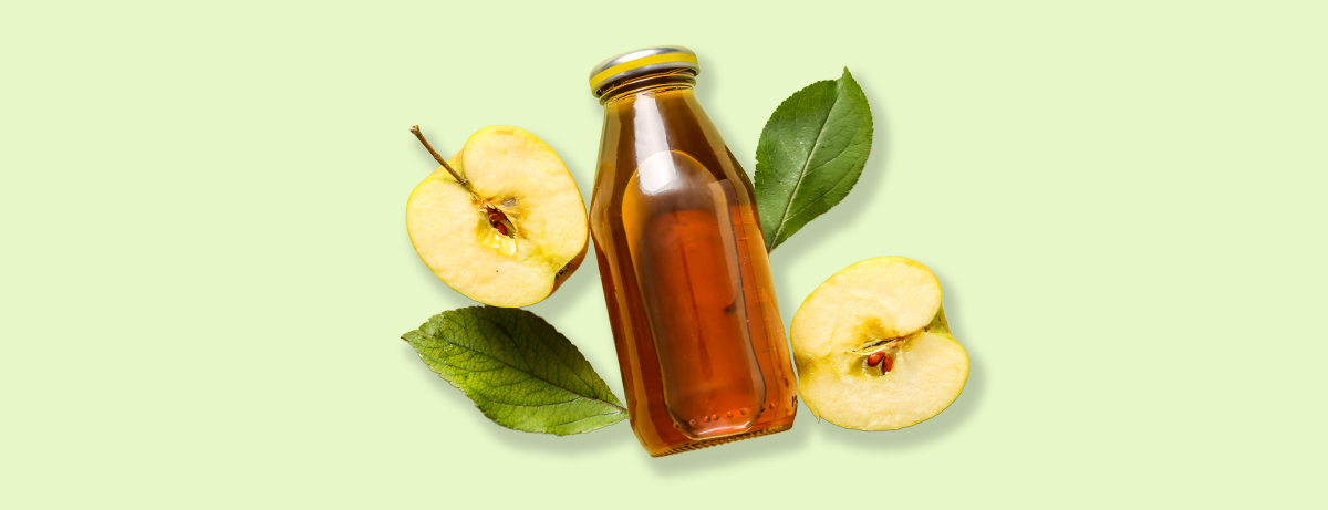 Apples next to glass of apple cider vinegar on a green background