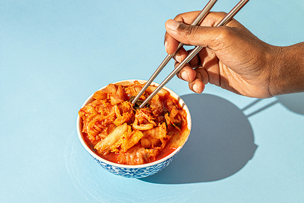 Hand holding chop sticks and a bowl of kimchi
