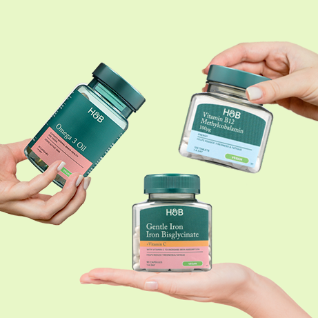 Hands holding 3x supplement bottles on green background
