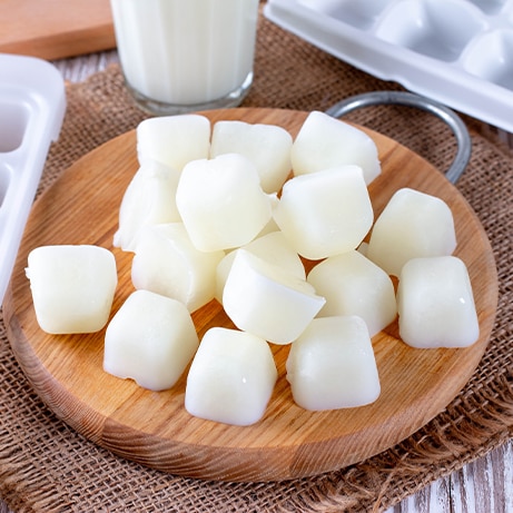 Milk ice cubes on a cutting board a white wooden table