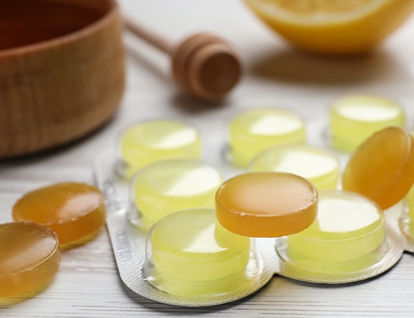 Many cough drops on white wooden table, closeup