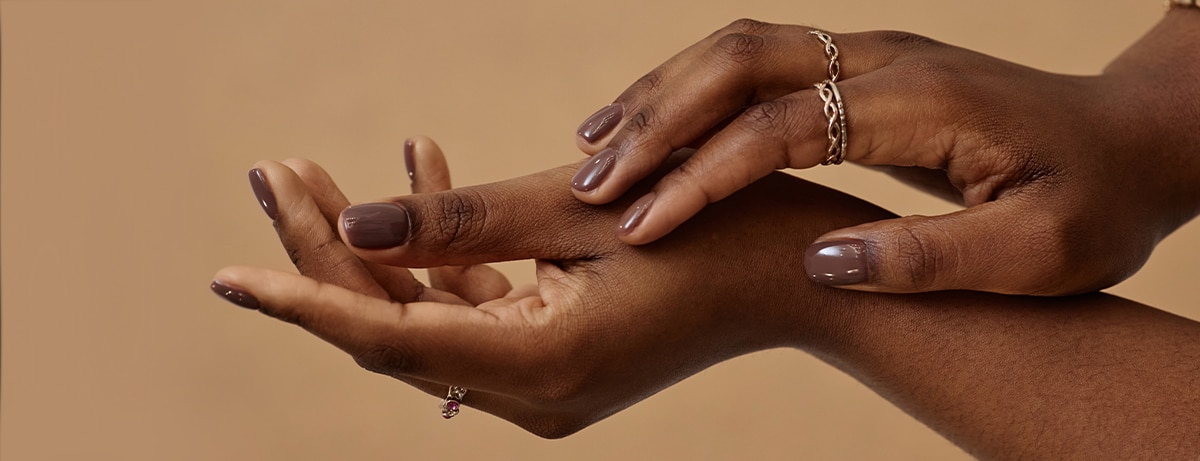 Vertical close up on female hands with soft touch gesture presenting perfect nude manicure. African American womans hands with healthy skin on beige background, skincare concept