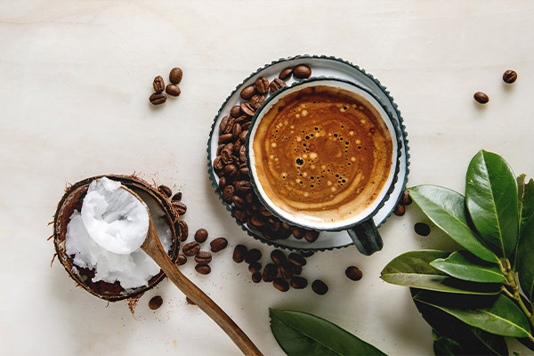 Bulletproof coffee. Keto diet coffee in blue ceramic cup with organic coconut cold press oil in wooden spoon with beans and green branch over white marble background. Flat lay, space
