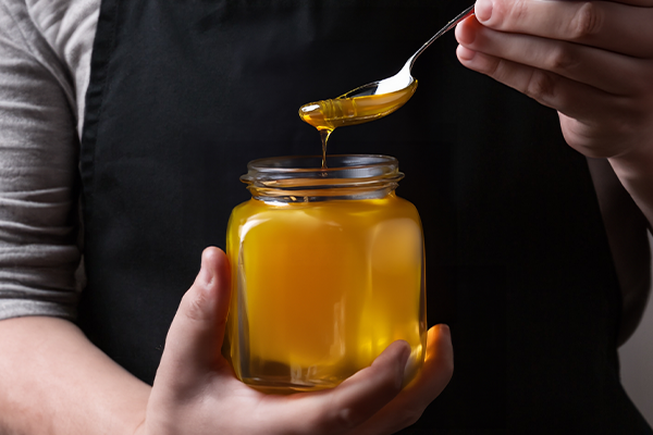 farmer pours a fresh harvest of honey into a glass jar. Organic Honey dripping, pouring from honey dipper in glasses bowl. Close-up