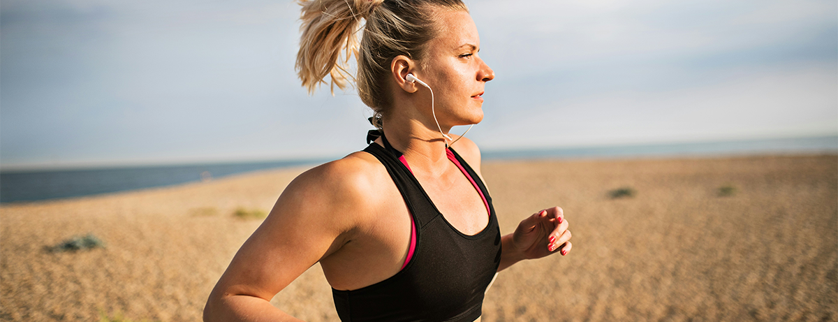 Woman running along the beach with blue sky. Woman is in fitness clothes and happy expression.