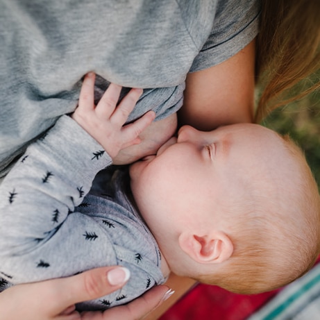 Breastfeeding baby. Mother breast feeding newborn boy sitting on grass in summer park. Concept of lactation infant, postpartum period, natural motherhood. Mom hug son on nature. Babywearing. Closeup.