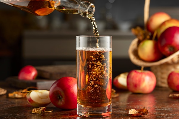 Apple cider is poured from a bottle into a glass. Fresh drink with apples on an old kitchen table.