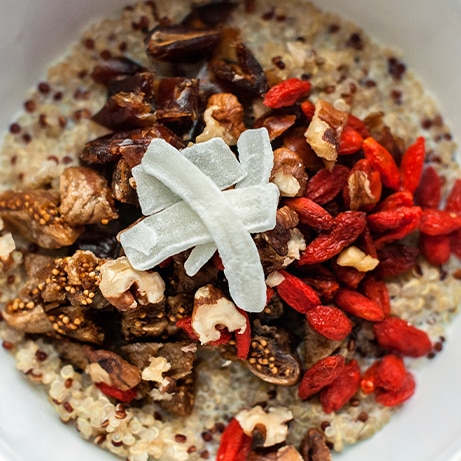 Healthy breakfast bowl. Milky quinoa porridge with goji, coconut, figs and nuts. Cup of cappuchino coffee. Selective focus, closeup view