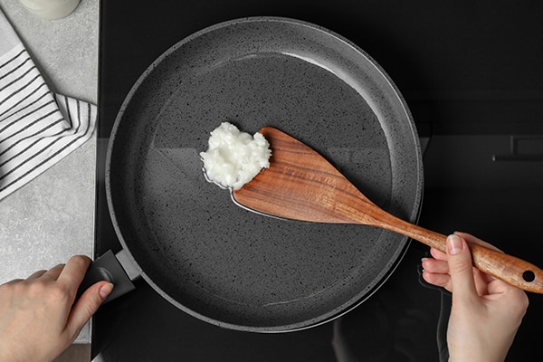 Woman cooking with coconut oil on induction stove, top view