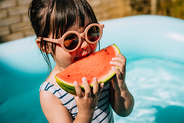 Child in outdoor swimming pool eating watermelon