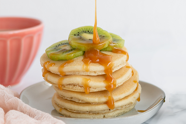 Honey being drizzled onto pancakes with kiwi