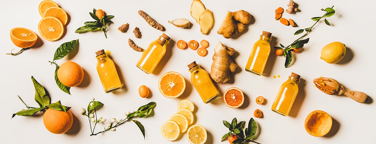 Immune boosting natural vitamin health defending drink to resist virus. Flat-lay of fresh turmeric, ginger and citrus juice shots over white background, top view. Vegan Immunity system booster