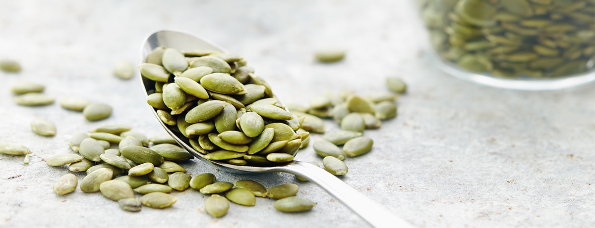 Pumpkin seeds on and beside spoon, close up
