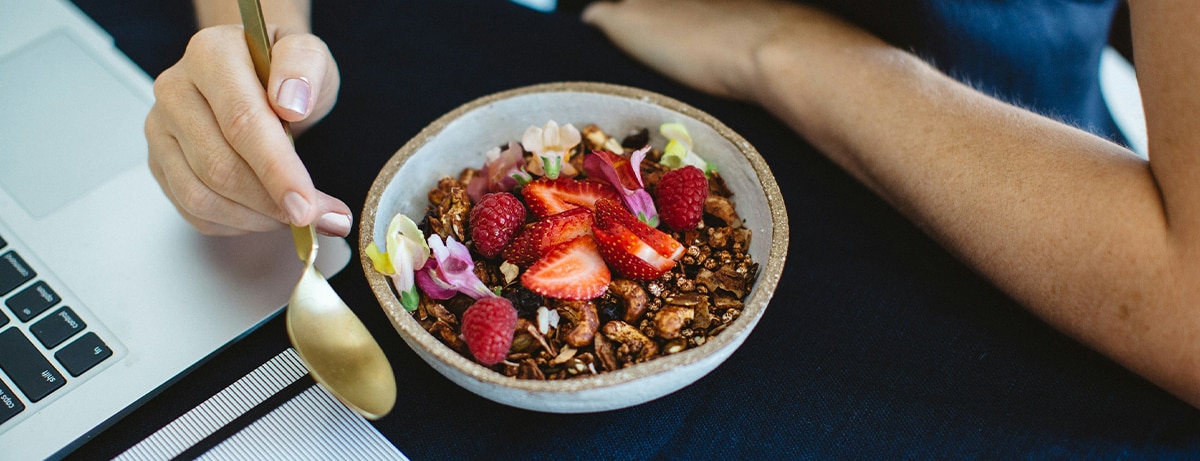 Female next to laptop eating a portion of strawberries and granola