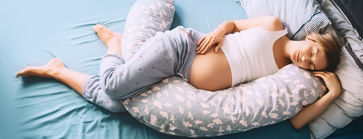 Pregnant female laying on bed in pyjamas asleep