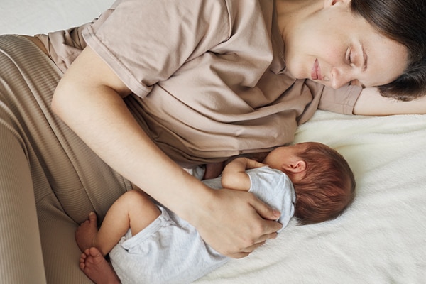Breastfeeding time. Cozy lactation. Caucasian beautiful mother breastfeeding her baby while lying on bed looking at her infant son with smile and love