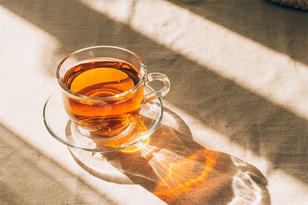 A cup of tea in glass cup and saucer illuminated by warm sunlight on a light table. Horizontal frame, copy space