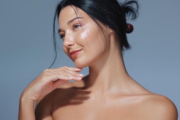 An elegant woman with natural makeup and glowing skin posing in a studio against a blue background. Perfect for beauty, skincare, and cosmetics promotions, this high-quality image features ample copy