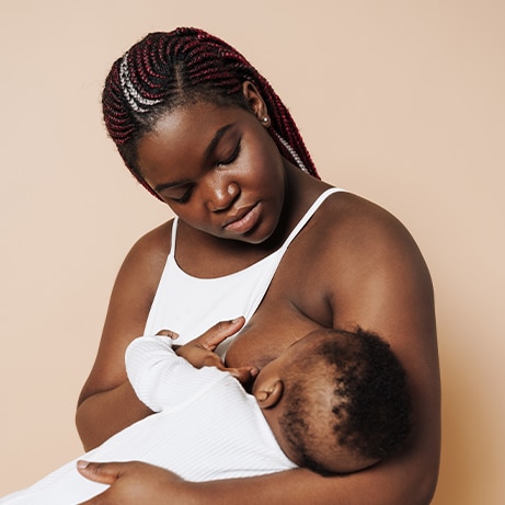 Beautiful african mother breastfeeding her newborn baby in white suit over isolated brown background