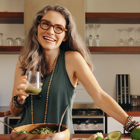 Healthy senior woman smiling while holding some green juice in her kitchen. Mature woman serving herself wholesome vegan food at home. Woman taking care of her aging body with a plant-based diet.