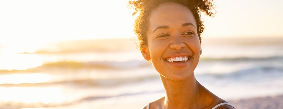 Smiling young black woman in beachwear enjoy sunset at beach. Satisfied beautiful girl with afro hair relaxing at beach during sunrise with copy space. African american woman daydreaming.