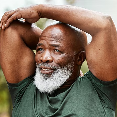 muscular older back man with white beard doing arm stretches in park for exercise