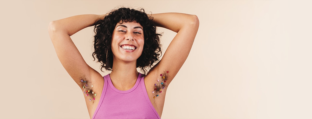 Happy young woman smiling at the camera while flaunting her confetti-decorated underarm hair. Body positive young woman making the choice not to shave. Cheerful young woman embracing her natural body.