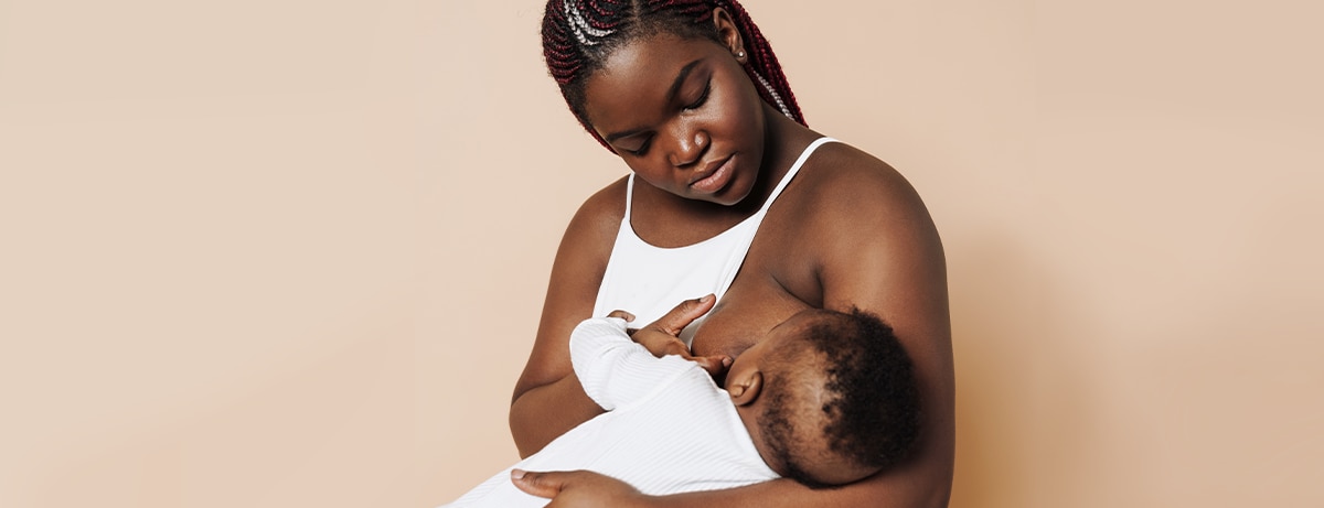 Beautiful african mother breastfeeding her newborn baby in white suit over isolated brown background