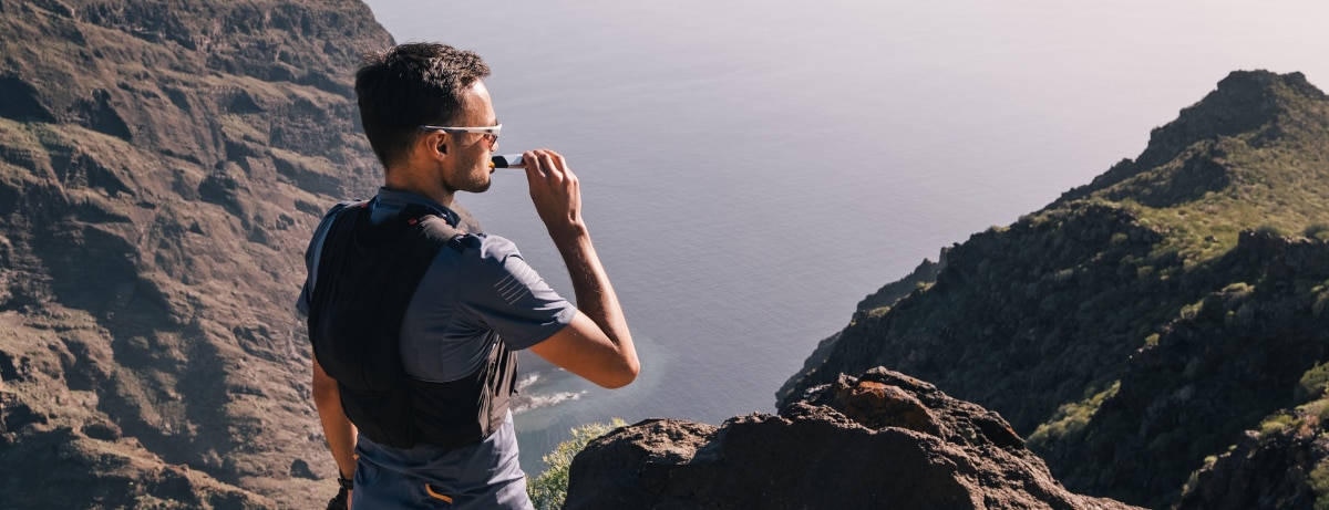 Portrait of young man drinking energy sports nutrition energy gel while sitting and resting after trail running on mountain peak