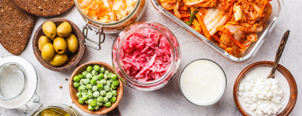 Probiotics food background. Kimchi, beet sauerkraut, sauerkraut, cottage cheese, olives, bread, chocolate, kefir and pickled cucumbers in glass jars, white background, top view.
