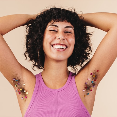 Happy young woman smiling at the camera while flaunting her confetti-decorated underarm hair. Body positive young woman making the choice not to shave. Cheerful young woman embracing her natural body.