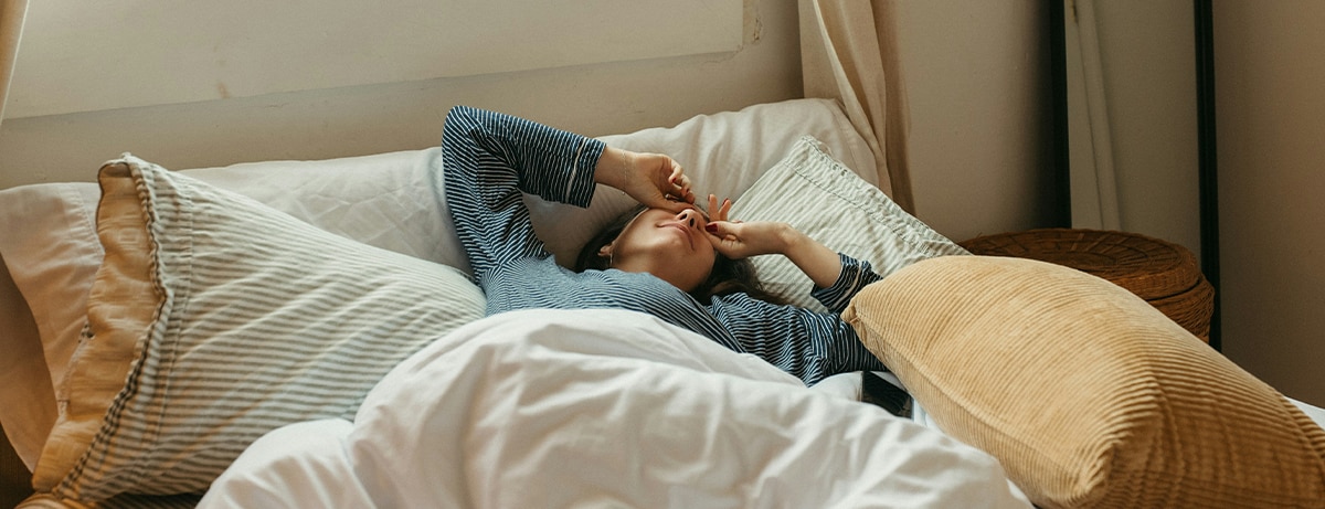 Female laying in bed, covering eyes