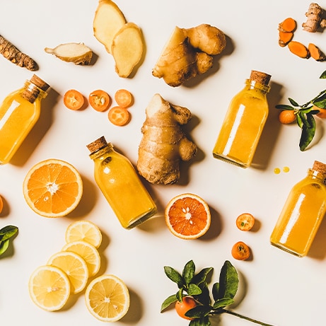 Immune boosting natural vitamin health defending drink to resist virus. Flat-lay of fresh turmeric, ginger and citrus juice shots over white background, top view. Vegan Immunity system booster