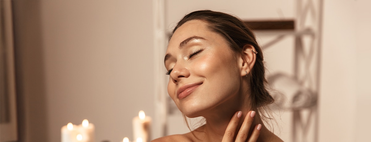 Portrait of a lovely young woman wrapped in a towel applying body cream at the spa center