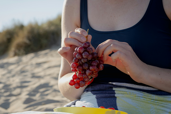 Female eating some purple grapes on the beach