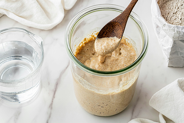Glass of sourdough in a bowl with a wooden spoon