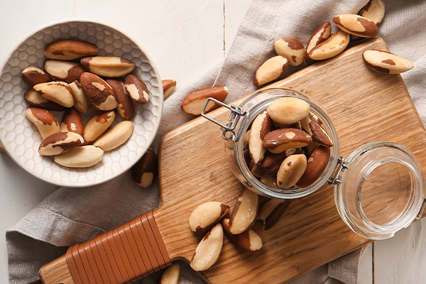 Bowl and jar with tasty Brazil nuts on white wooden background