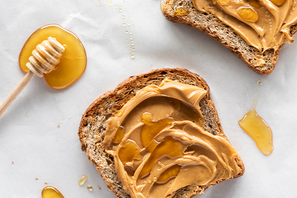 Close up view of a piece of toast covered with creamy peanut butter and honey, ready for eating.