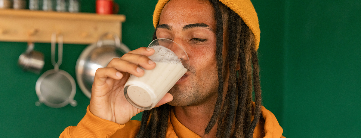 man with yellow hat in kitchen drinking yoghurt liquid