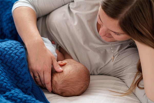 happy young woman feeds breast milk and hugs baby. a mother is breastfeeding a newborn baby while lying on the bed. Concept of newborn lactation. The child eats milk before going to bed. Side view.