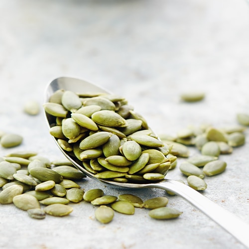 Pumpkin seeds on and beside spoon, close up