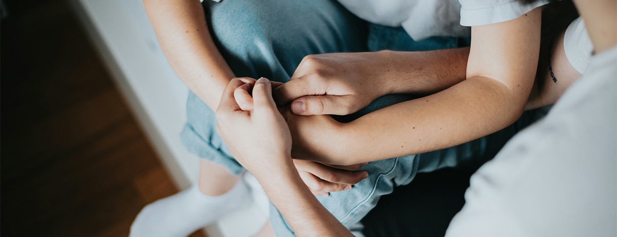 Two people sitting on bed, close up of hands holding