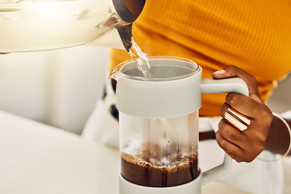 Female hands making morning coffee to enjoy with breakfast, pouring hot water from kettle in a kitchen.