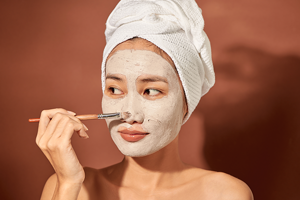Attracitve young Asian woman applying clay mask on her facee. Spa and wellness, skin care product concept.