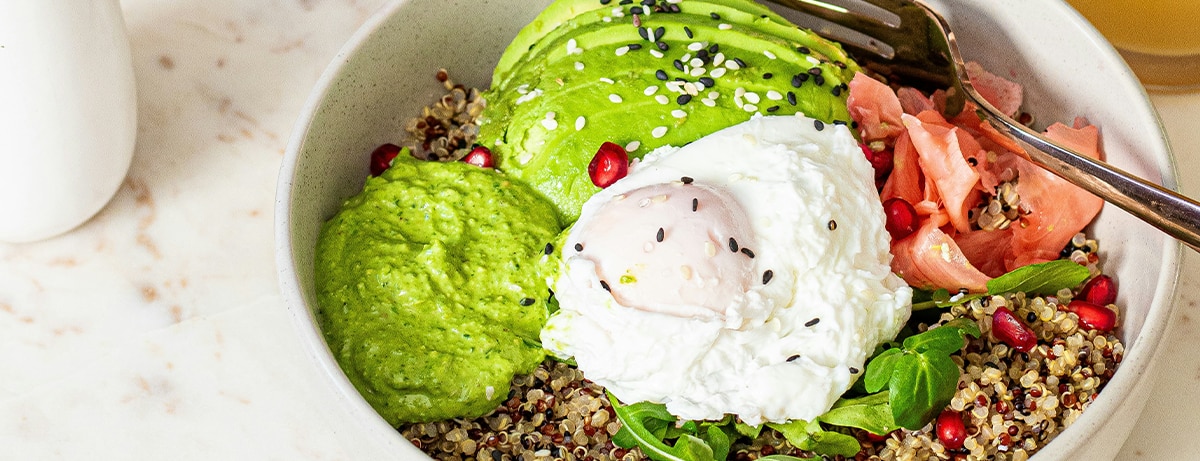 Quinoa healthy bowl with salmon, avocado, poached egg, pink ginger, green dresing and pomegranate with orange juice.