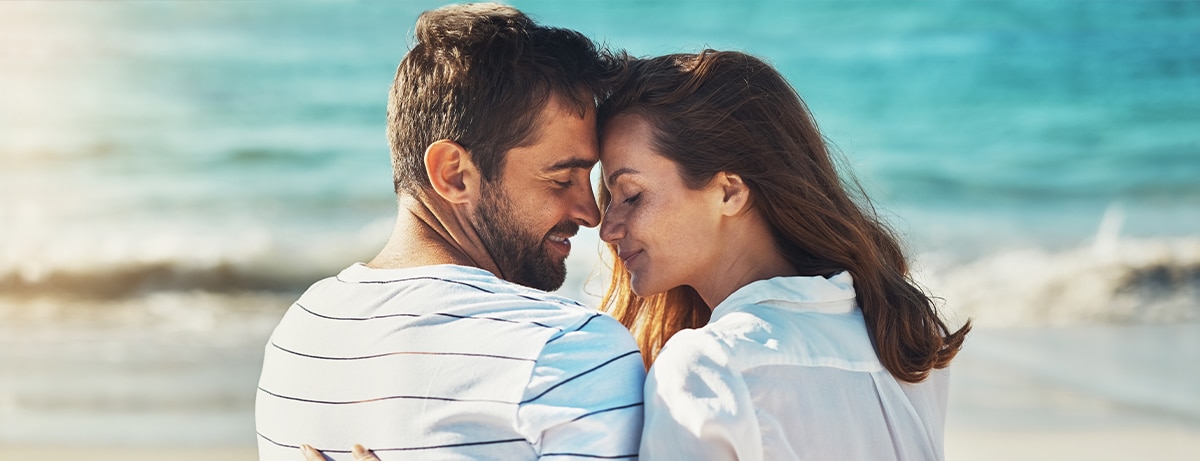 Hug, couple and relax on beach for love, commitment and bonding on summer vacation for honeymoon. Man, woman and back view together by ocean for romantic holiday, affection and weekend with embrace.
